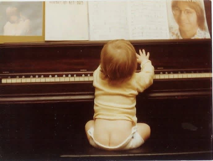 A 1970s Kodachrome photo of Chris LoPresto as a baby, reaching up to the keys of a mahogany upright piano