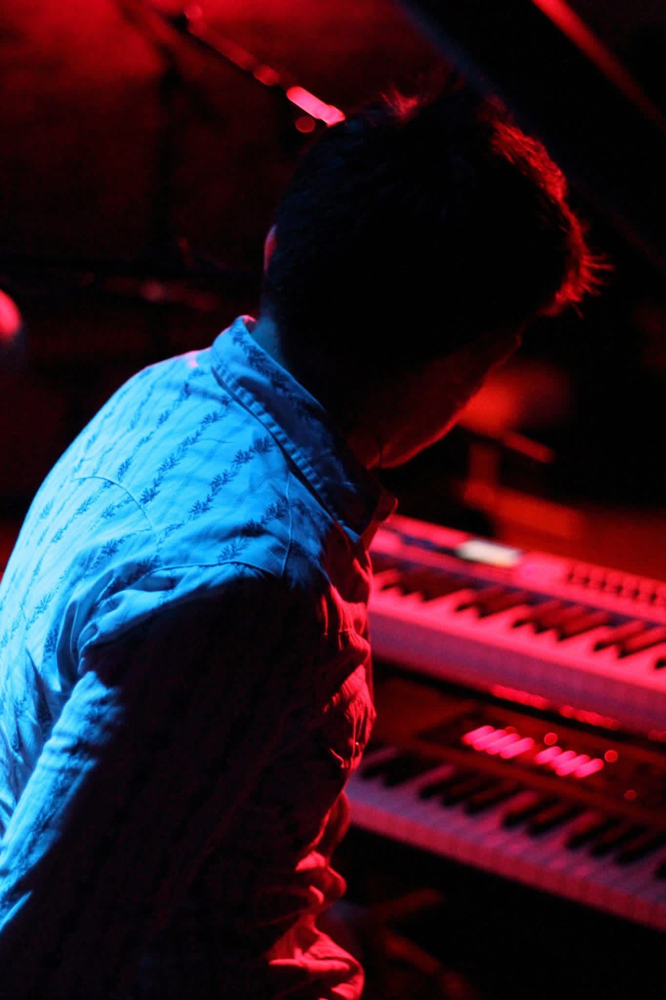 Chris LoPresto head down at the keys under a deep red stage wash